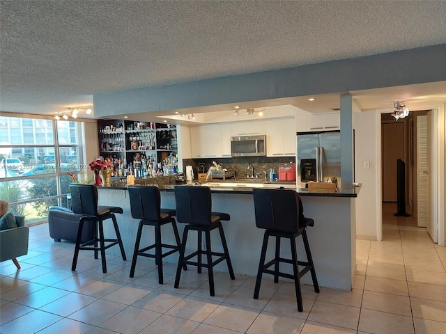 kitchen featuring white cabinets, tasteful backsplash, kitchen peninsula, appliances with stainless steel finishes, and light tile patterned flooring