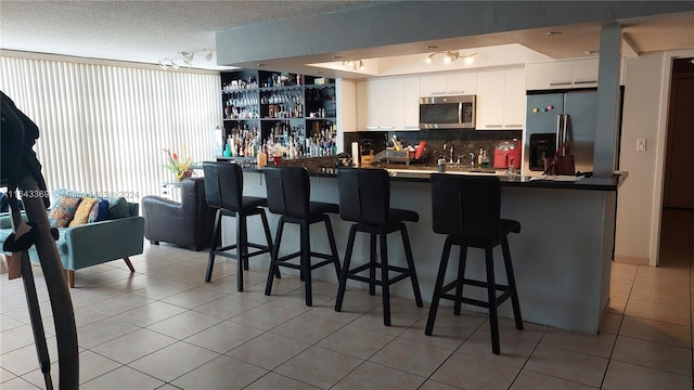 kitchen with refrigerator, white cabinetry, kitchen peninsula, light tile patterned flooring, and a kitchen bar