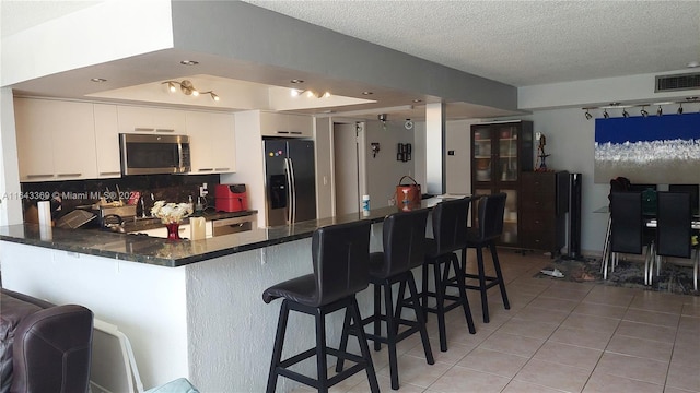 kitchen with a kitchen breakfast bar, kitchen peninsula, black fridge with ice dispenser, white cabinetry, and decorative backsplash