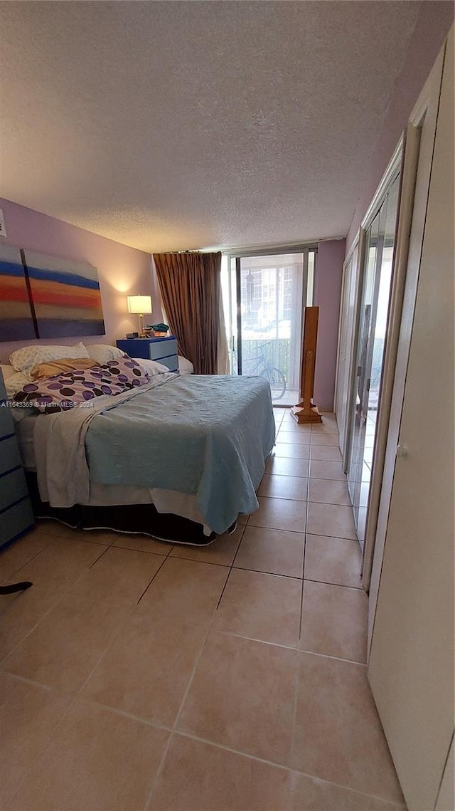 tiled bedroom with a wall of windows, access to exterior, and a textured ceiling