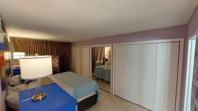 bedroom featuring light tile patterned floors, a textured ceiling, and two closets