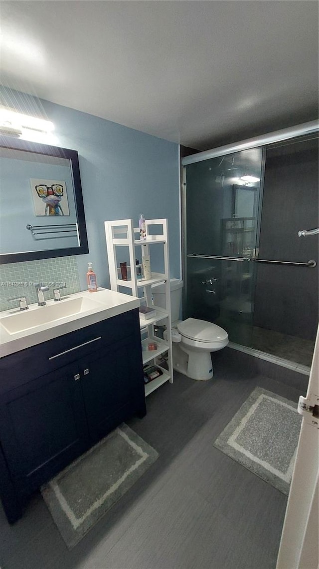 bathroom featuring toilet, vanity, backsplash, hardwood / wood-style flooring, and a shower with shower door