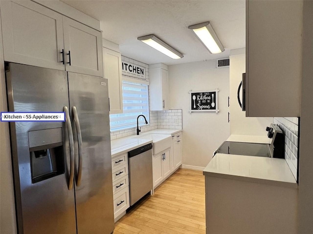 kitchen with sink, appliances with stainless steel finishes, decorative backsplash, light hardwood / wood-style floors, and white cabinets