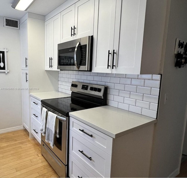 kitchen with appliances with stainless steel finishes, decorative backsplash, light wood-type flooring, and white cabinets