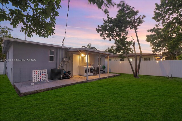 back house at dusk featuring a patio, cooling unit, a yard, and washer and dryer