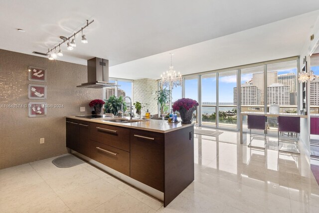 kitchen featuring sink, dark brown cabinetry, wall chimney exhaust hood, track lighting, and light tile patterned floors