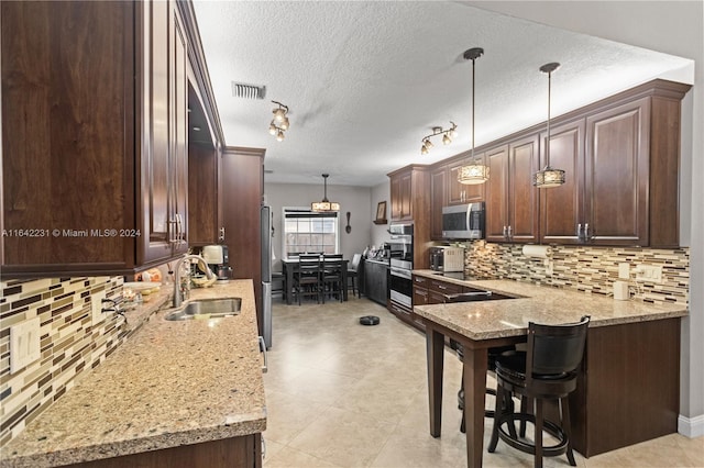 kitchen featuring decorative light fixtures, stainless steel appliances, tasteful backsplash, sink, and kitchen peninsula