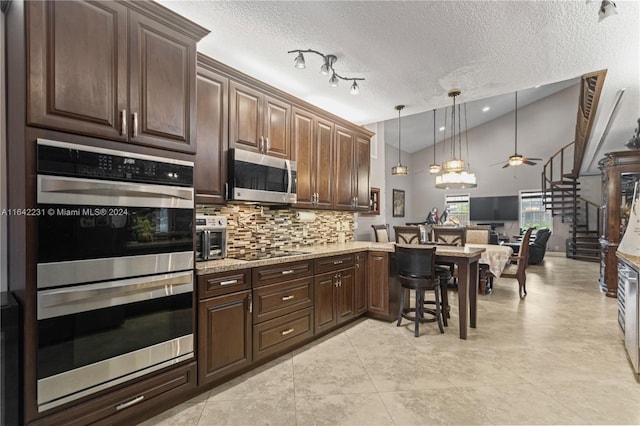 kitchen with appliances with stainless steel finishes, light stone countertops, a textured ceiling, ceiling fan, and a breakfast bar