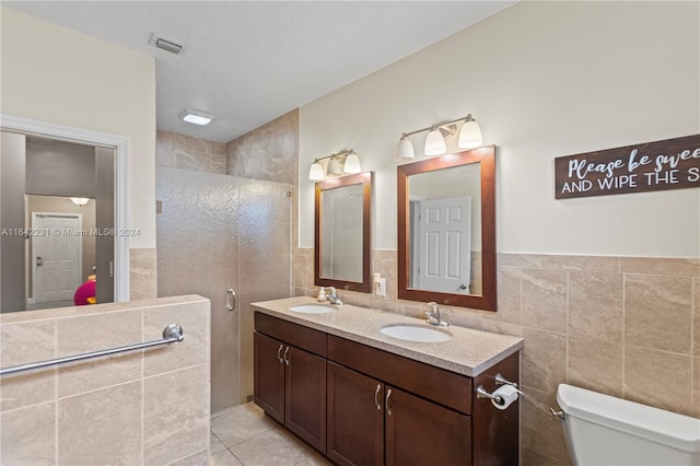 bathroom with toilet, tile patterned floors, tile walls, dual bowl vanity, and a textured ceiling