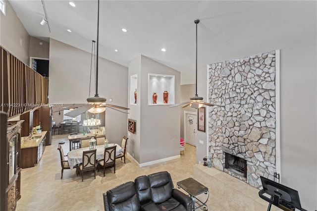 tiled living room with ceiling fan, rail lighting, a stone fireplace, and high vaulted ceiling