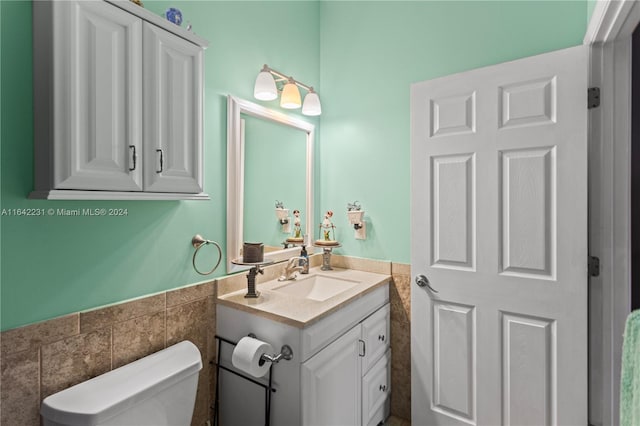 bathroom with toilet, vanity, and tile walls