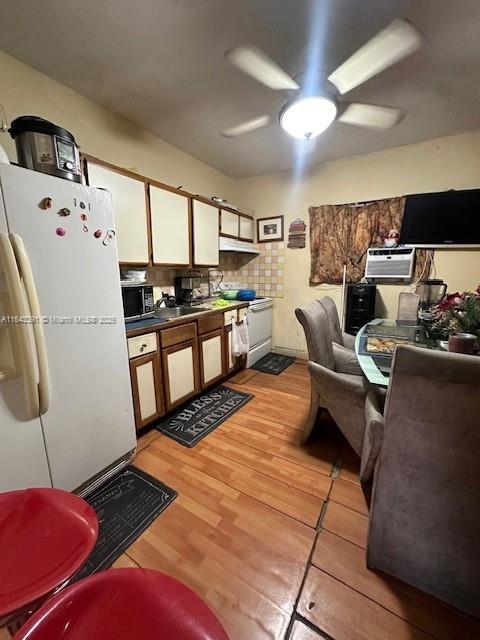 kitchen featuring white fridge, a wall mounted AC, light wood-type flooring, ceiling fan, and white cabinetry