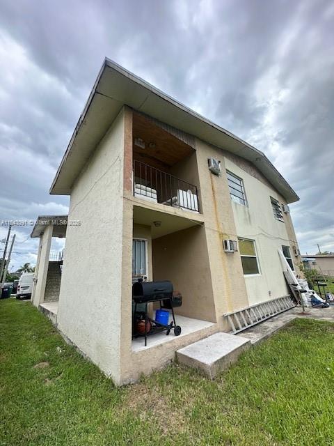 rear view of property with a balcony, a wall mounted AC, and a yard