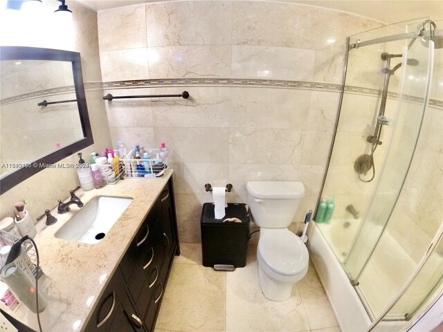 full bathroom featuring combined bath / shower with glass door, vanity, tile patterned floors, tile walls, and toilet