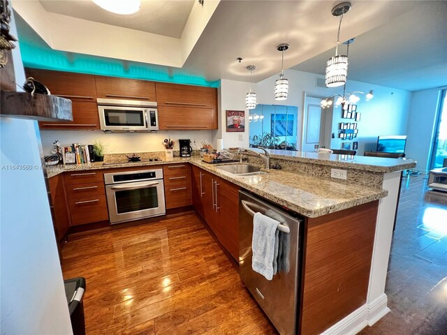 kitchen with hanging light fixtures, kitchen peninsula, sink, dark wood-type flooring, and appliances with stainless steel finishes