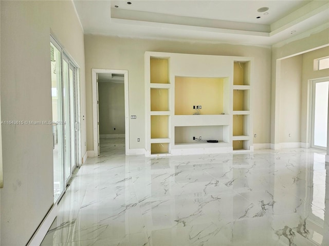 unfurnished living room with built in features, a raised ceiling, light tile patterned flooring, and a wealth of natural light