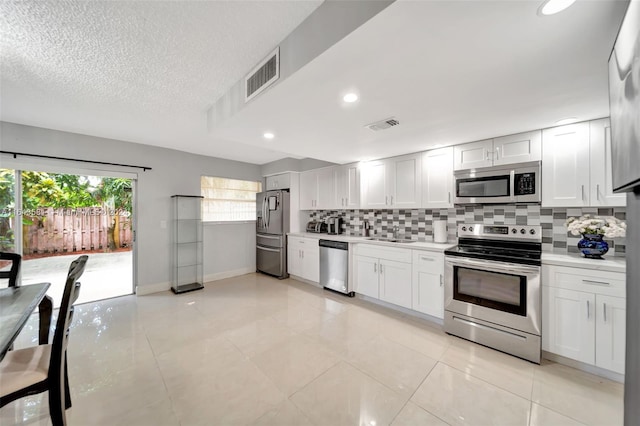 kitchen featuring appliances with stainless steel finishes, white cabinetry, light tile patterned floors, and backsplash