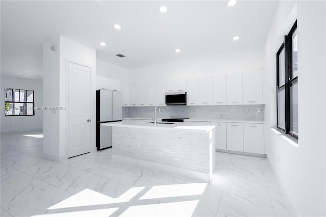 kitchen with white cabinets, freestanding refrigerator, a sink, marble finish floor, and backsplash