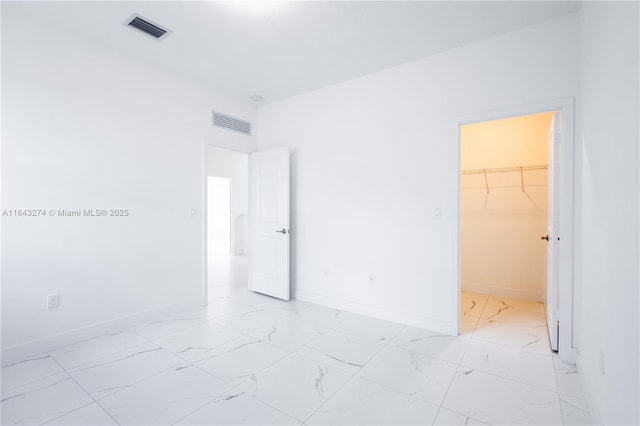 unfurnished bedroom with marble finish floor, baseboards, visible vents, and a walk in closet