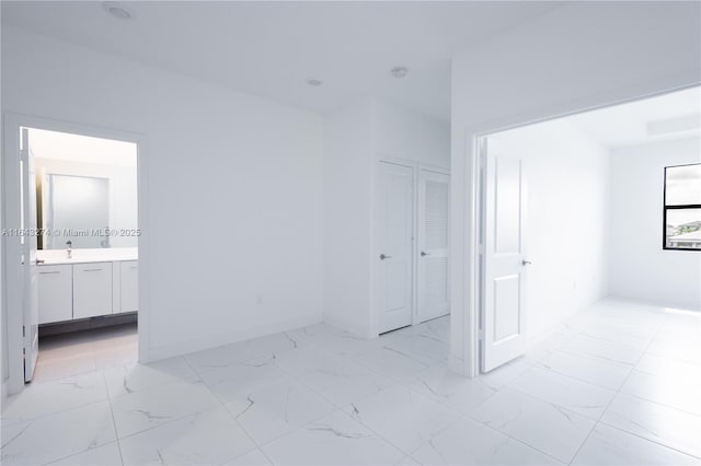 unfurnished bedroom featuring marble finish floor, connected bathroom, baseboards, and a sink