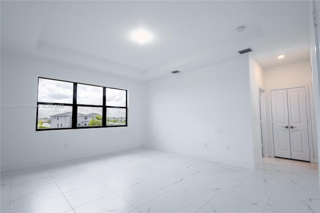 spare room featuring a tray ceiling, marble finish floor, visible vents, and baseboards