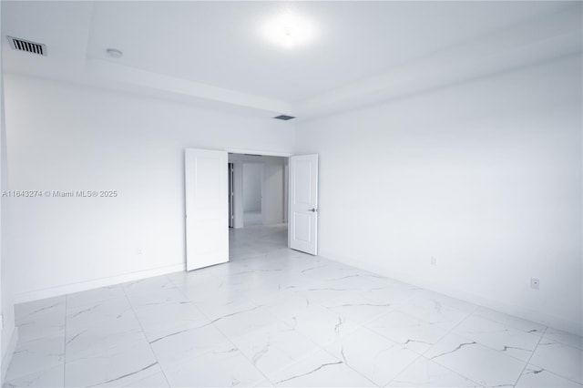 unfurnished room featuring marble finish floor, a tray ceiling, visible vents, and baseboards