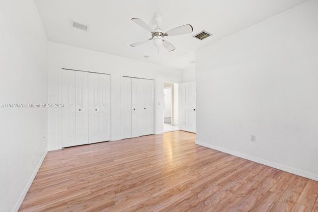 unfurnished bedroom featuring ceiling fan, light hardwood / wood-style floors, and two closets