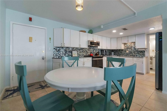 kitchen with light tile patterned flooring, range, tasteful backsplash, a textured ceiling, and white cabinets