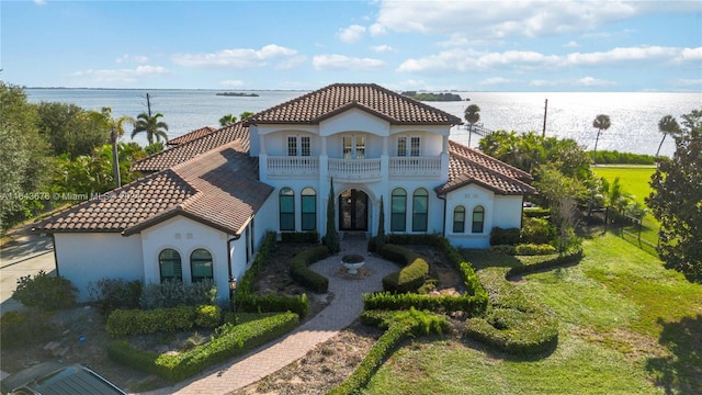 mediterranean / spanish-style home featuring a balcony, french doors, a water view, and a front lawn