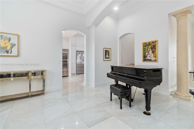 misc room with a towering ceiling, crown molding, ornate columns, and wine cooler