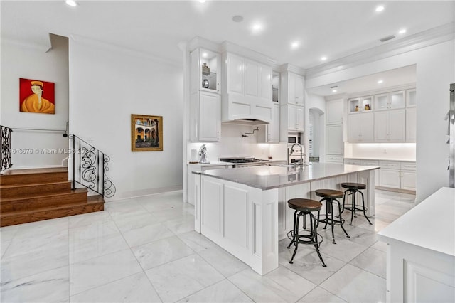 kitchen featuring ornamental molding, a kitchen bar, premium range hood, a center island with sink, and white cabinets