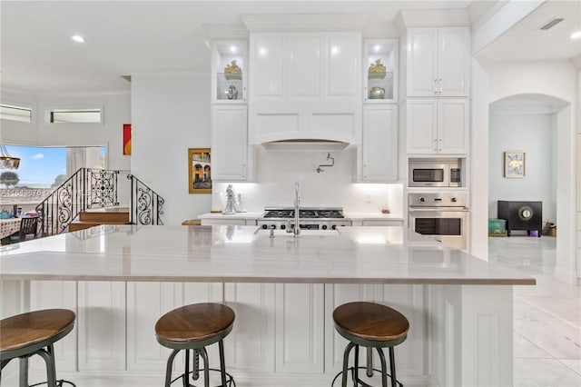 kitchen with custom range hood, appliances with stainless steel finishes, a breakfast bar, a large island with sink, and white cabinets