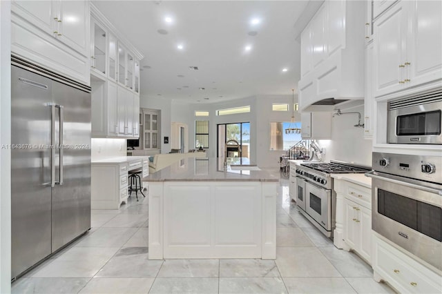 kitchen with built in appliances, light tile patterned floors, white cabinetry, and a kitchen island with sink