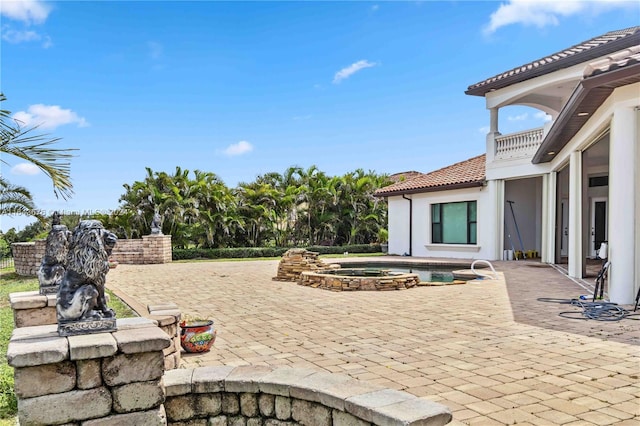 view of patio featuring a balcony and an in ground hot tub