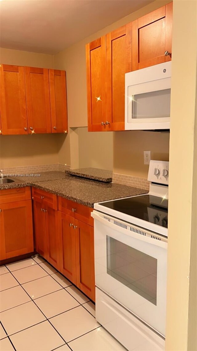 kitchen featuring white appliances, light tile patterned floors, and dark stone countertops