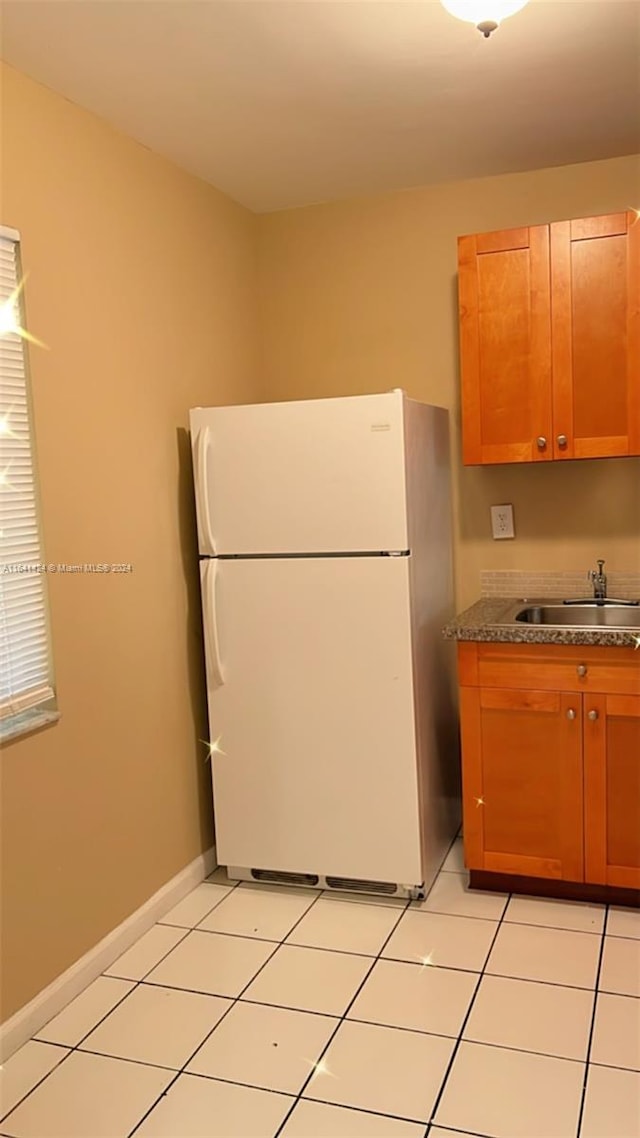 kitchen with white refrigerator, stone countertops, sink, and light tile patterned floors