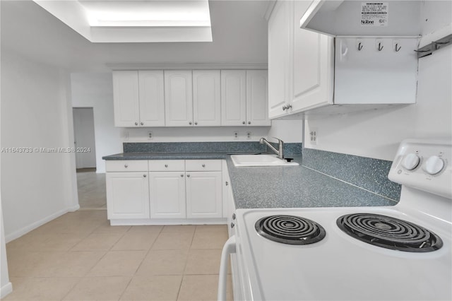 kitchen with light tile patterned floors, range, sink, and white cabinetry