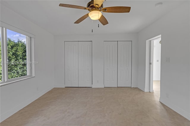 unfurnished bedroom featuring ceiling fan, multiple closets, and light tile patterned floors