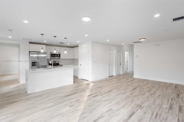 kitchen featuring sink, an island with sink, appliances with stainless steel finishes, decorative light fixtures, and white cabinetry