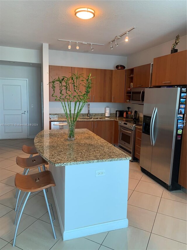 kitchen with a breakfast bar, appliances with stainless steel finishes, light stone counters, light tile patterned floors, and rail lighting