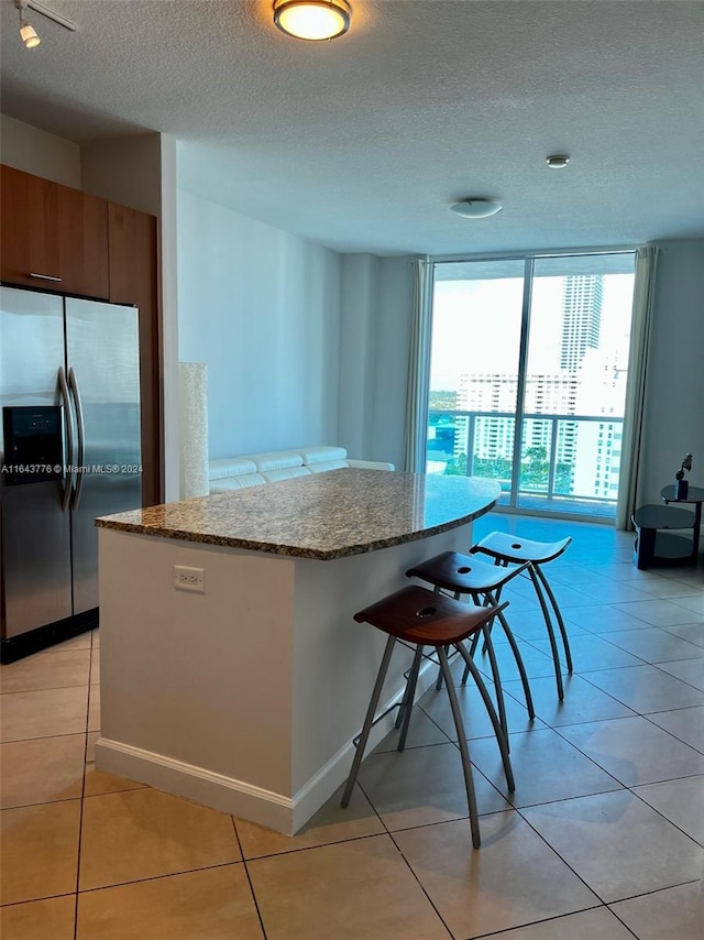 kitchen featuring light tile patterned flooring, stainless steel fridge, light stone counters, and a textured ceiling