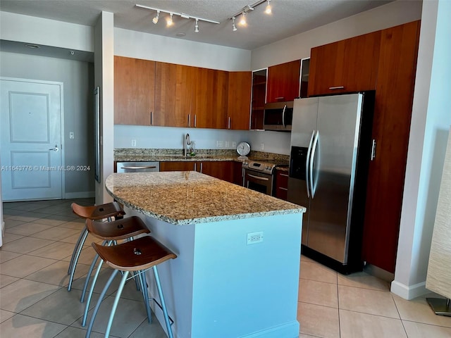 kitchen with a kitchen island, a breakfast bar, light stone counters, rail lighting, and stainless steel appliances