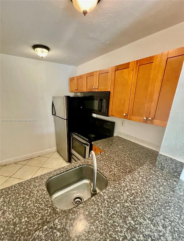 kitchen with sink, stainless steel appliances, light tile patterned floors, and dark stone countertops