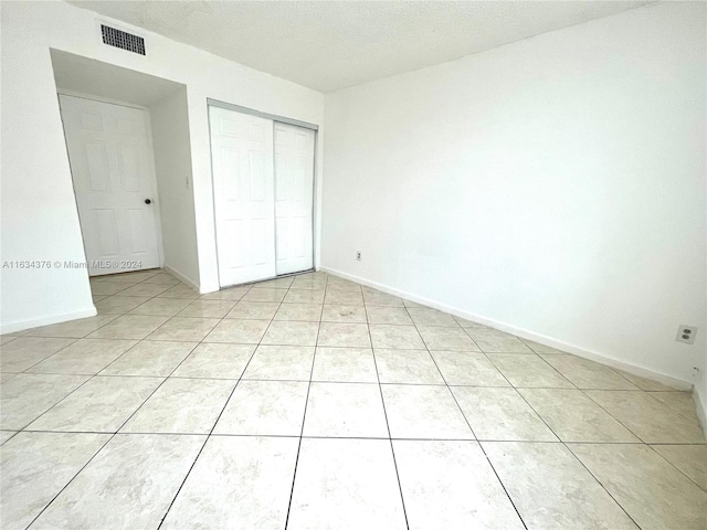 unfurnished bedroom with a textured ceiling, a closet, and light tile patterned floors