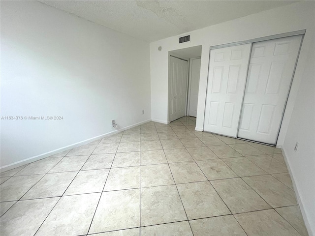 unfurnished bedroom featuring a textured ceiling, a closet, and light tile patterned floors