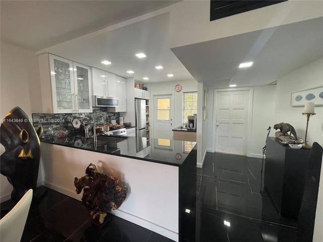 kitchen featuring appliances with stainless steel finishes, backsplash, white cabinetry, dark tile patterned flooring, and kitchen peninsula