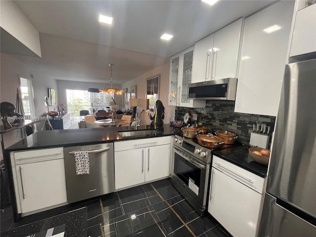 kitchen with sink, appliances with stainless steel finishes, dark tile patterned floors, kitchen peninsula, and white cabinets