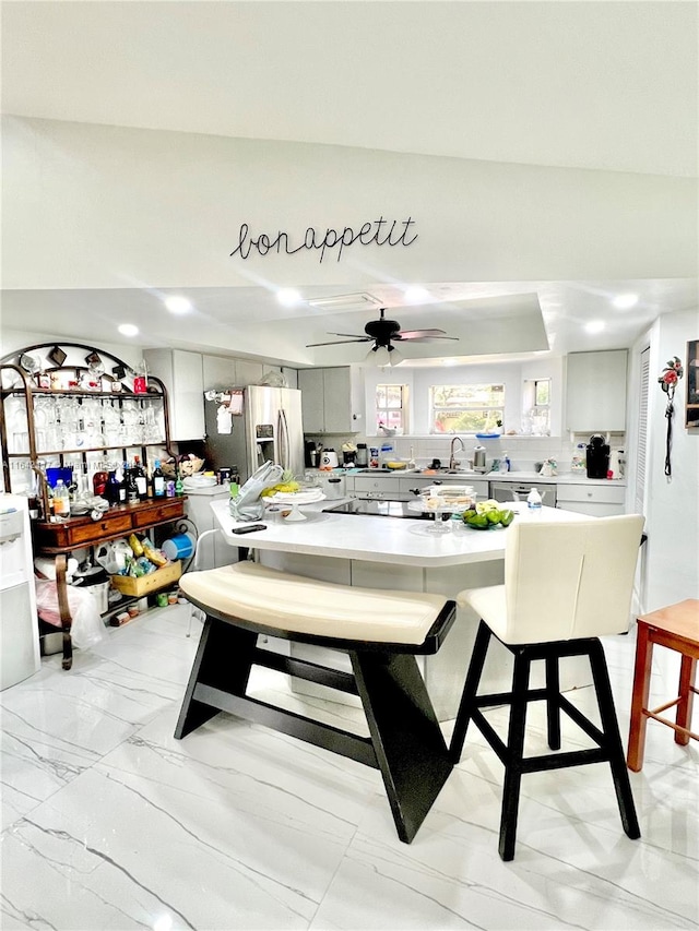 interior space featuring ceiling fan, a breakfast bar, appliances with stainless steel finishes, light tile patterned floors, and sink