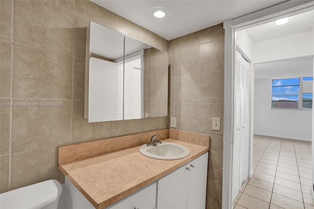 bathroom with tile patterned floors, toilet, tile walls, and vanity