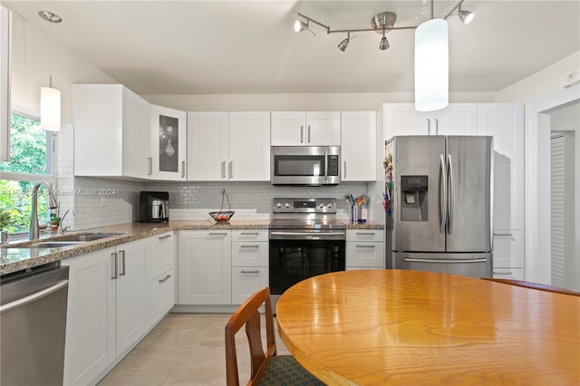 kitchen featuring decorative backsplash, white cabinets, track lighting, appliances with stainless steel finishes, and light stone counters